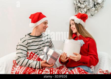 Young couple or brother with sister sitting on the sofa in their living room under Christmas while wearing cozy winter jumpers and exchanging their Ch Stock Photo