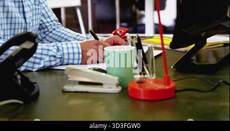 Writing man's hands holding pen on paper at corporate office desk, with stapler mug lamp Stock Photo