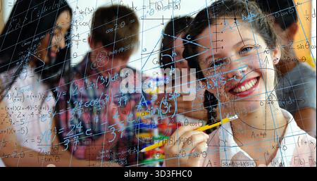 Smiling teen girl holding yellow pencil writing math equations on glass board in class, copy space Stock Photo