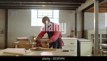 Sanding mature carpenter wearing apron smoothing wooden plank at carpentry shop, sander, lumber Stock Photo