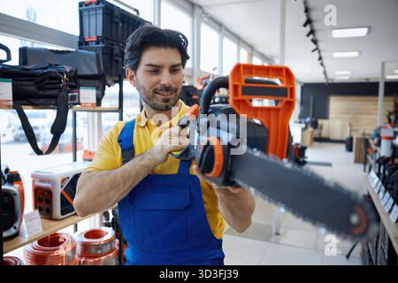 Worker is standing in a store holding a chainsaw tool Stock Photo