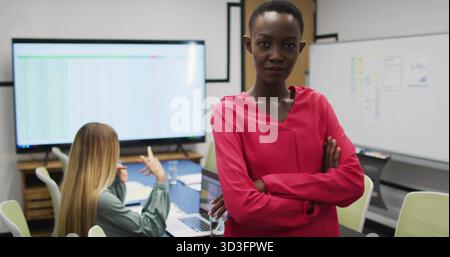 Reviewing figures, woman wearing red blouse crossing arms in office with large display, copy space Stock Photo