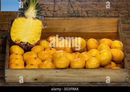 fresh oranges and half pineapple in wooden crate Stock Photo