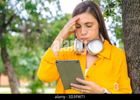Young caucasian woman frustrated while using digital tablet outdoors in park Stock Photo