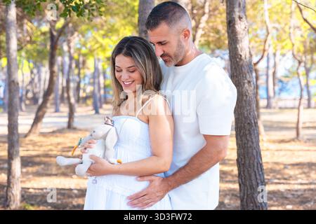 Pregnant couple outdoors holding soft toy, love and tenderness moment. Stock Photo