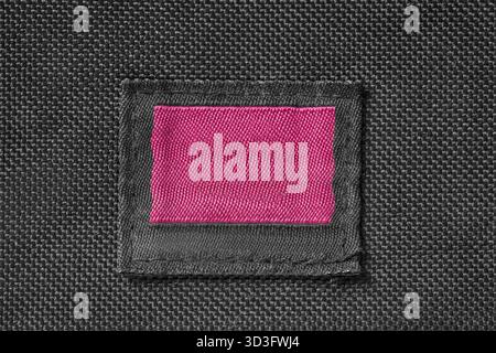 Empty pink patch clothes label stitched on black fabric background Stock Photo