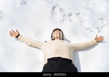A joyful woman lies on her back in the snowy Pyrenees, basking in the winter chill. Embracing leisure and adventure, she enjoys a moment of pure relax Stock Photo