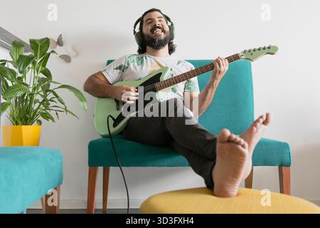 A man sits comfortably at home, playing his guitar and enjoying his musical session. He is immersed in the melody, showcasing passion and relaxation i Stock Photo