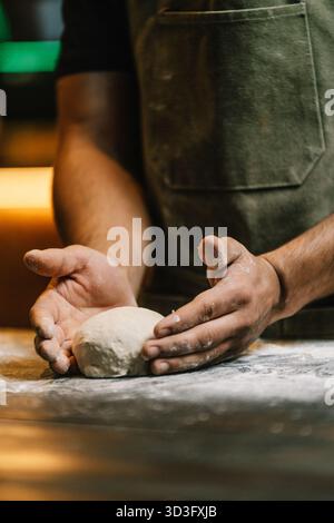 A baker is kneading fresh dough on a floured wooden surface, focusing on the hands and dough. The scene evokes a sense of craftsmanship and dedication Stock Photo