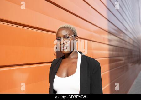 Businesswoman and CEO posing confidently by a modern orange wall, showcasing her leadership and professionalism. Dressed in formal attire, setting a p Stock Photo