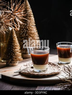 A glass of layered coffee with condensed milk sits on a woven coaster atop a wooden tray. The background features decorative golden Christmas trees ad Stock Photo