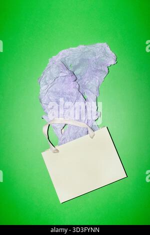 Paper shopping bag with white handles and crumpled tissue paper on a vibrant green background, perfect for representing eco friendly gifting or retail Stock Photo