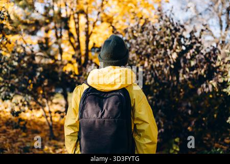 A man is captured from behind, wearing a bright yellow raincoat and a beanie, enjoying a peaceful autumn day. Vibrant fall foliage surrounds him, crea Stock Photo