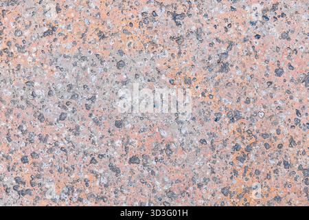 Close-up of a rough concrete surface featuring speckled patterns in gray and orange hues. The textured finish highlights the intricacies of natural we Stock Photo