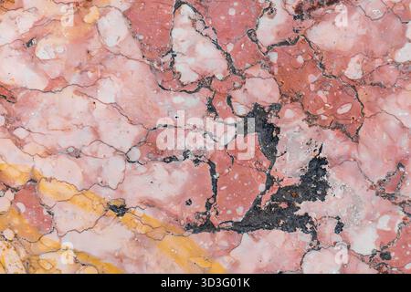 Close-up of a textured marble surface featuring a fusion of pink and yellow hues, accentuated by contrasting dark veins, offering an intricate and org Stock Photo