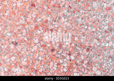 Close-up of a terrazzo surface featuring vibrant pink and red stone fragments set in a light gray cement background. The textured pattern creates an a Stock Photo