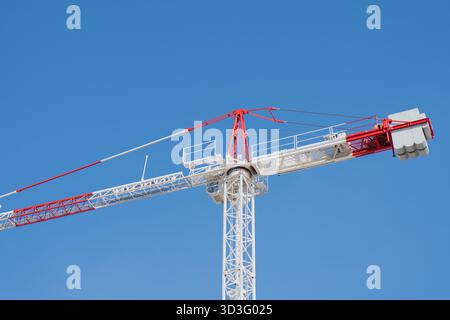 From below a tall, white and red tower crane stands against a clear blue sky on a construction site, illustrating modern engineering and urban develop Stock Photo