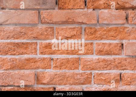 A close-up image of a brick wall displaying a rustic texture and orange-brown hue. The aged, worn surface adds an industrial, vintage charm to the des Stock Photo