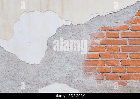An image showcasing a textured wall with exposed red bricks, partially covered by worn-out plaster and gray stucco. The surface reveals an appealing m Stock Photo