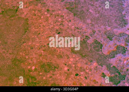 Close-up of a textured rocky surface with reddish and green hues, showcasing natural formations and embedded pebbles. Ideal for backgrounds or design Stock Photo