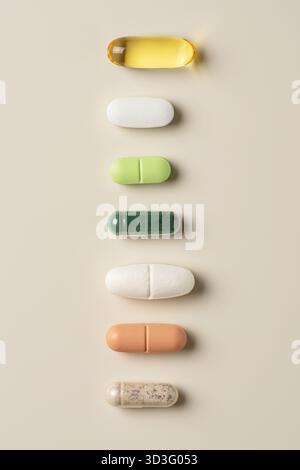 Top view of assorted pills on a beige background. Includes capsules in various colors such as yellow, white, green, orange, and brown. Represents supp Stock Photo