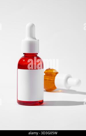 A red and an amber serum bottle with white droppers are displayed on a white background. These dropper bottles, used for skincare, enhance your beauty Stock Photo