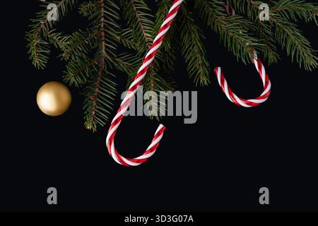 Festive New Year scene featuring red and white candy sticks hanging alongside pine tree branches on a stark black background, creating a striking seas Stock Photo