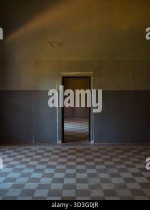 An abandoned interior space showcasing a checkered floor and a doorway leading to another dimly lit room, evoking a sense of mystery and historic aban Stock Photo