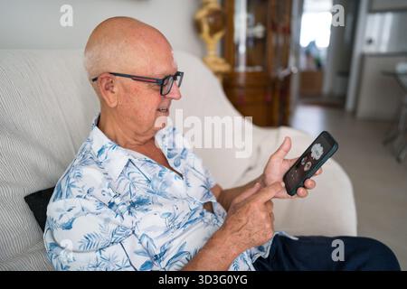 An elderly man enjoys connecting on an online dating app using his smartphone, illustrating modern relationships and digital lifestyles in senior comm Stock Photo