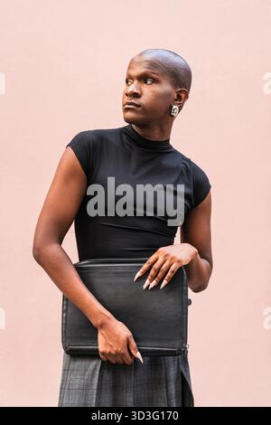 Young LGBTQ man stands confidently against a neutral background. His outfit combines elegance and style, showcasing individuality and modern fashion. Stock Photo