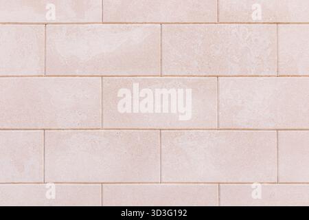 The image showcases a beige tiled wall, perfectly aligned in horizontal rows. The bricks display a textured surface with subtle weathering, adding a n Stock Photo
