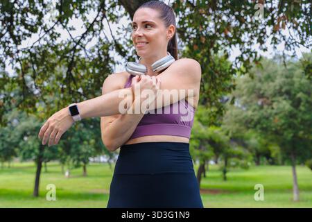 Sporty woman stretching arm across chest outdoors in park before fitness workout Stock Photo