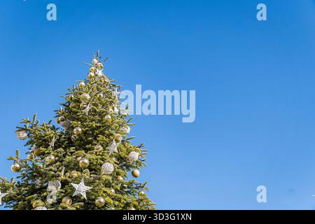 A stunning Christmas tree embellished with sparkling ornaments stands tall under a clear blue sky in Aosta. The festive decorations add a touch of mag Stock Photo