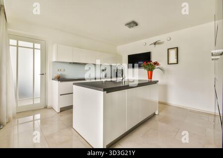 A stylish modern kitchen featuring sleek white cabinetry, elegant countertops, and a vibrant floral centerpiece, creating a bright and inviting atmosp Stock Photo