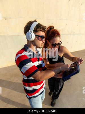 LGBT couple enjoying a vibrant lifestyle as they share a fun moment with a tablet outdoors. Embracing tech and connection, they represent a modern, jo Stock Photo