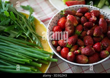 A vibrant display of a bowl filled with fresh strawberries next to a plate of green onions and arugula, arranged on a checkered tablecloth, showcasing Stock Photo