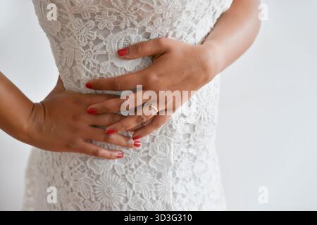 A close up shot of hands elegantly clasped against an intricate lace dress. The woman red nail polish complements the delicate floral patterns, exudin Stock Photo