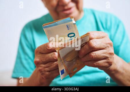 Cropped unrecognizable image of an elderly man at home counting euro bills, focusing on his hands as he organizes the currency, reflecting financial m Stock Photo