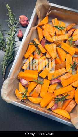 Raw sweet potatoes seasoned with rosemary and garlic, just to be baked. Healthy and vegetarian food. Overhead view. Stock Photo