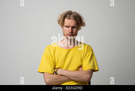 Confident young man in yellow shirt crossing arms and looking determined in studio portrait Stock Photo