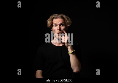 Surprised man in black shirt with wide eyes and shocked expression under dramatic light Stock Photo