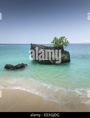 Aerial view of the dark, rugged rocks contrast with the serene turquoise waters and golden sands of the beach, Bali, Indonesia. Stock Photo