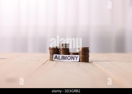 Paper note with word Alimony and stacked coins on wooden table Stock Photo