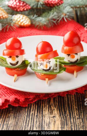 New Year's food made of cheese, mozzarella and basil on skewers, in the shape of snowmen, close-up on a plate on the table. Vertical Stock Photo