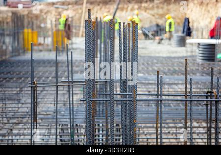 Steel reinforcement rods arranged at a city construction site with workers in safety gear visible in the background under daylight. Stock Photo