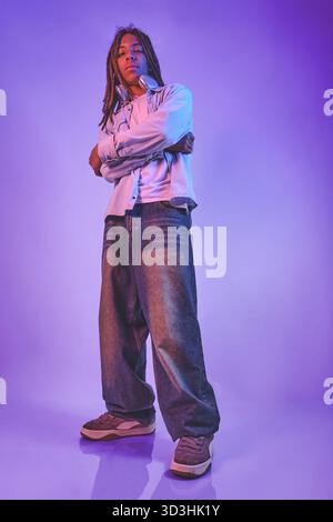 Young man with dreadlocks and headphones standing confidently against a vibrant purple background Stock Photo