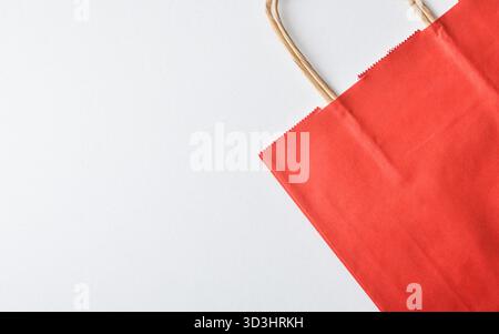 Detail of an empty, folded red paper shopping bag with brown braided paper handles on a white background. Top view. Stock Photo