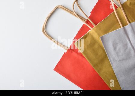 Empty, folded red, gold, and silver paper shopping bags with brown twisted paper handles isolated on a white background. Top view. Stock Photo
