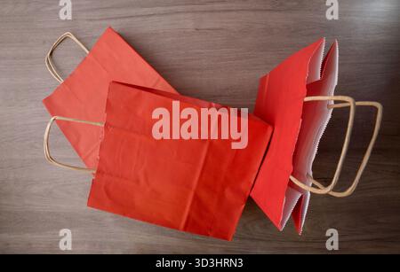 Pack of empty red paper shopping bags with brown twisted paper handles on a wooden table. Top view. Stock Photo