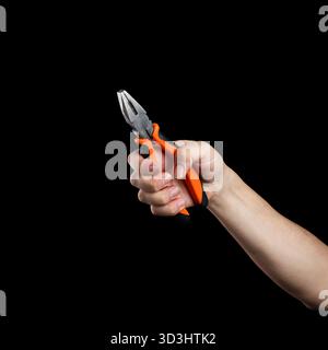 A man's hand grips a pair of orange-handled pliers, a tool for DIY or repair, isolated on a solid black background. Stock Photo
